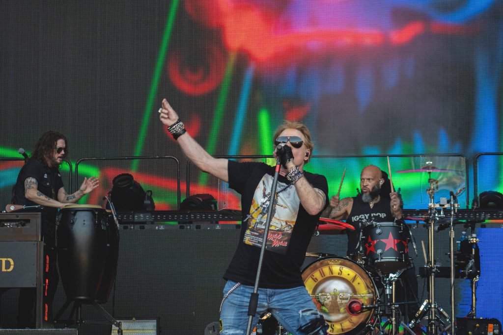 Axl Rose vibrant concert performance with aviators and Guns N Roses drum kit background wallpaper
