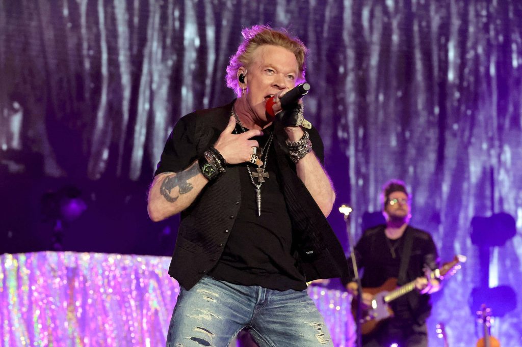 Axl Rose singing live in black vest and jeans on vibrant purple stage backdrop rock concert Wallpaper