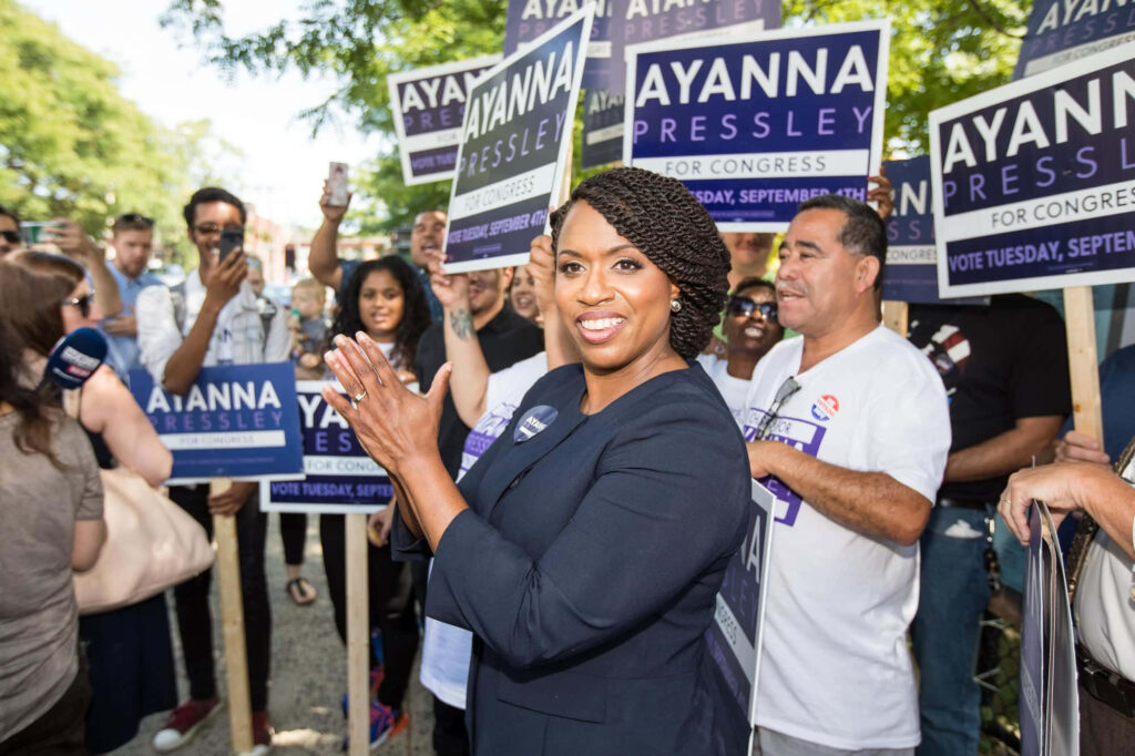 Ayanna Pressley smiles applauding at outdoor campaign stop with enthusiastic supporters and signs Wallpaper