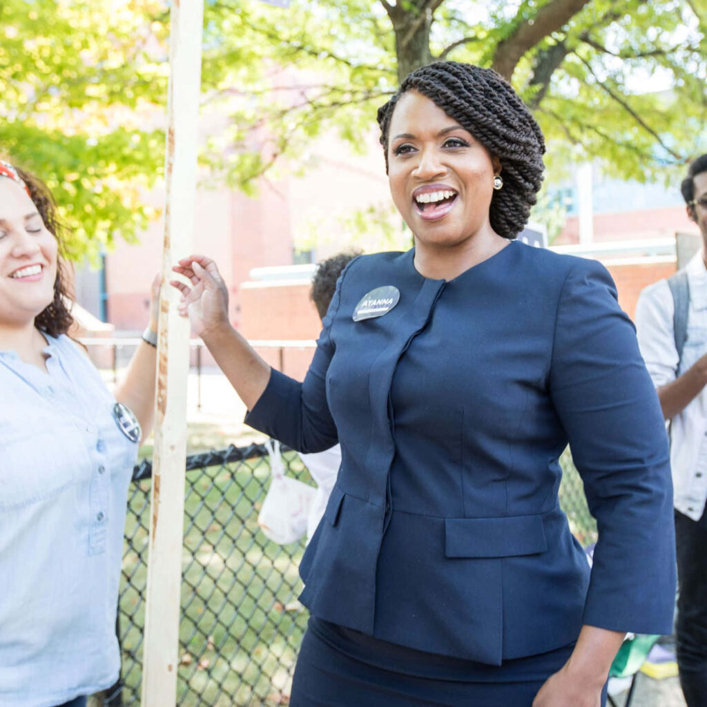 Ayanna Pressley smiling and engaging with supporters outdoors during her lively campaign event Wallpaper