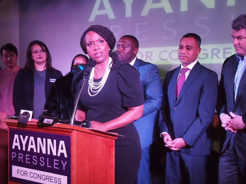 U.S. Representative Ayanna Pressley speaking passionately at podium with supporters and colleagues Wallpaper