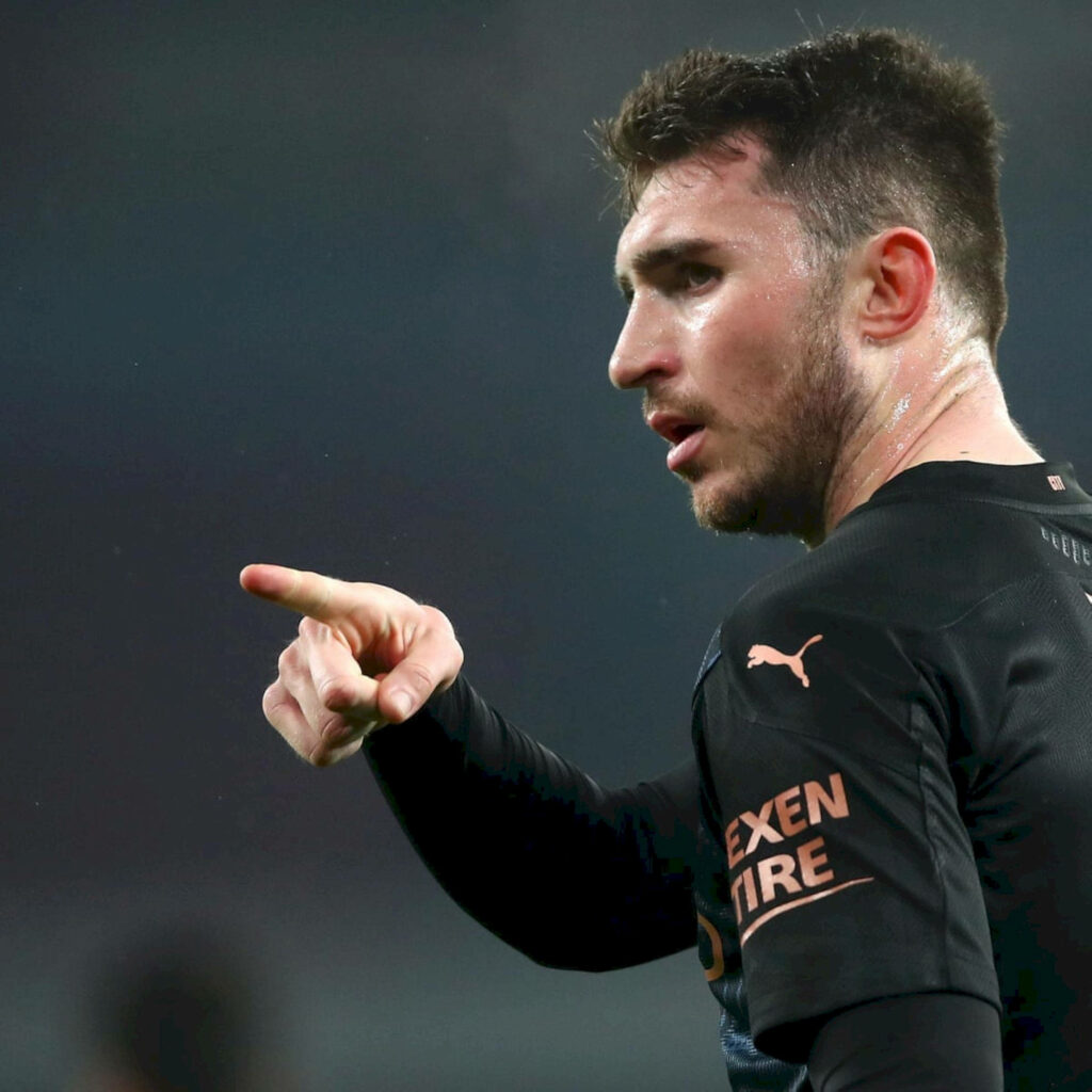 Aymeric Laporte in football kit confidently pointing sideways in dynamic soccer wallpaper background