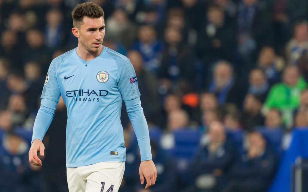 Aymeric Laporte in Manchester City kit focused walking across field during competitive football match Wallpaper