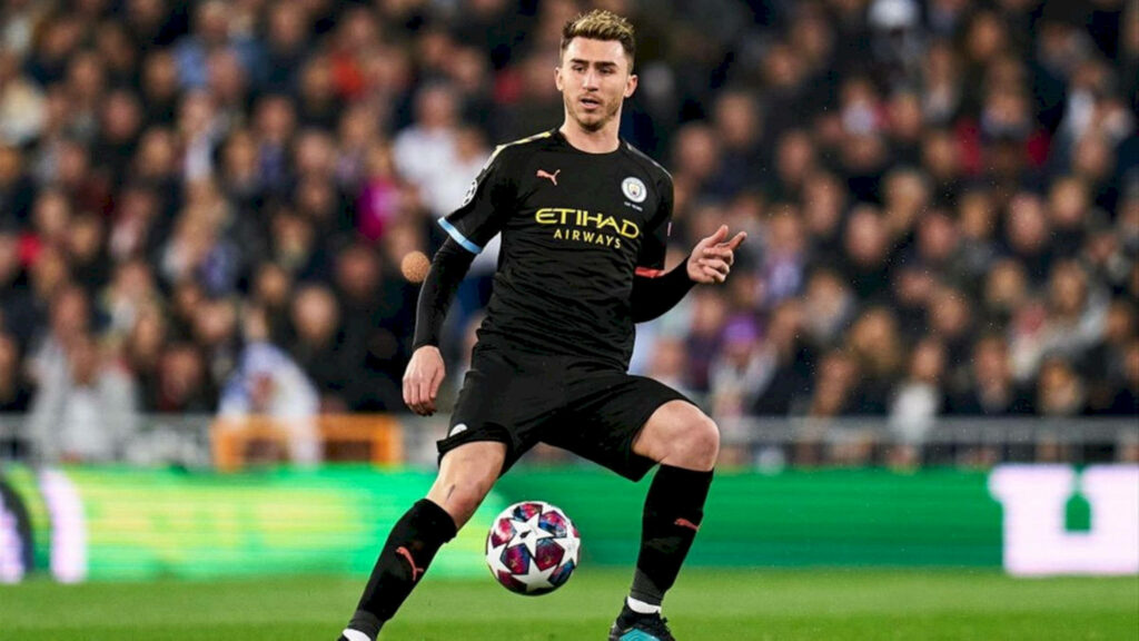 Aymeric Laporte controlling football between legs in Manchester City kit with crowd behind Wallpaper