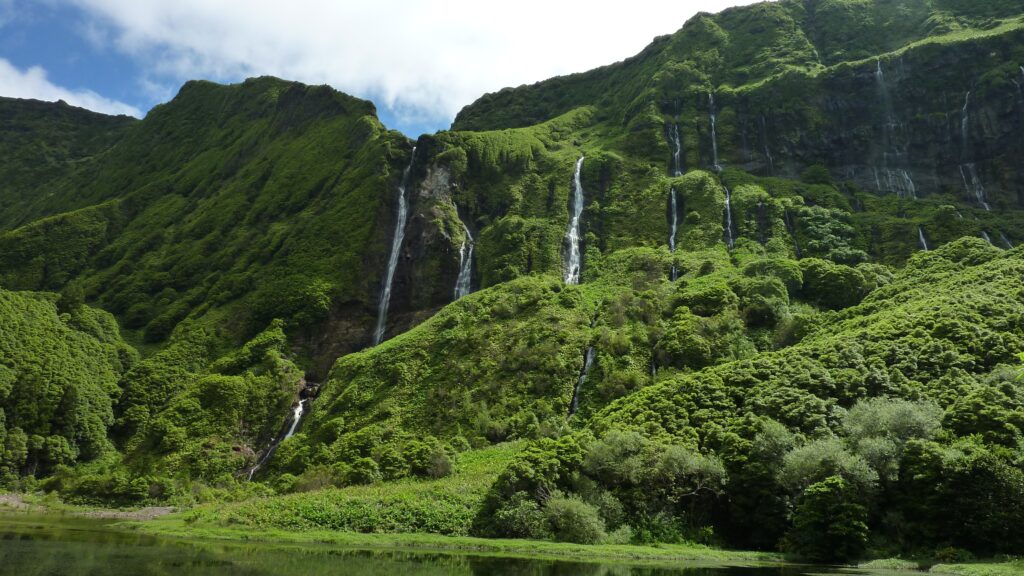 Lush Azores waterfalls cascading green cliffs with dense trees reflected in calm water wallpaper