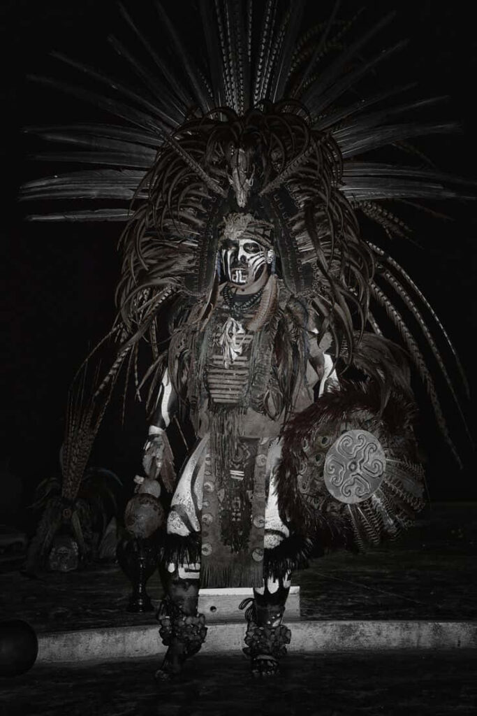Aztec warrior in elaborate feathered costume with traditional ornaments in dark wallpaper background