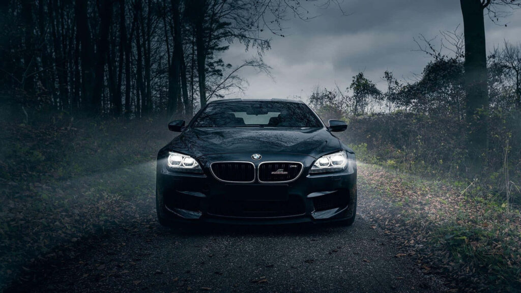 BMW driving through misty forest road at night with headlights on wallpaper background