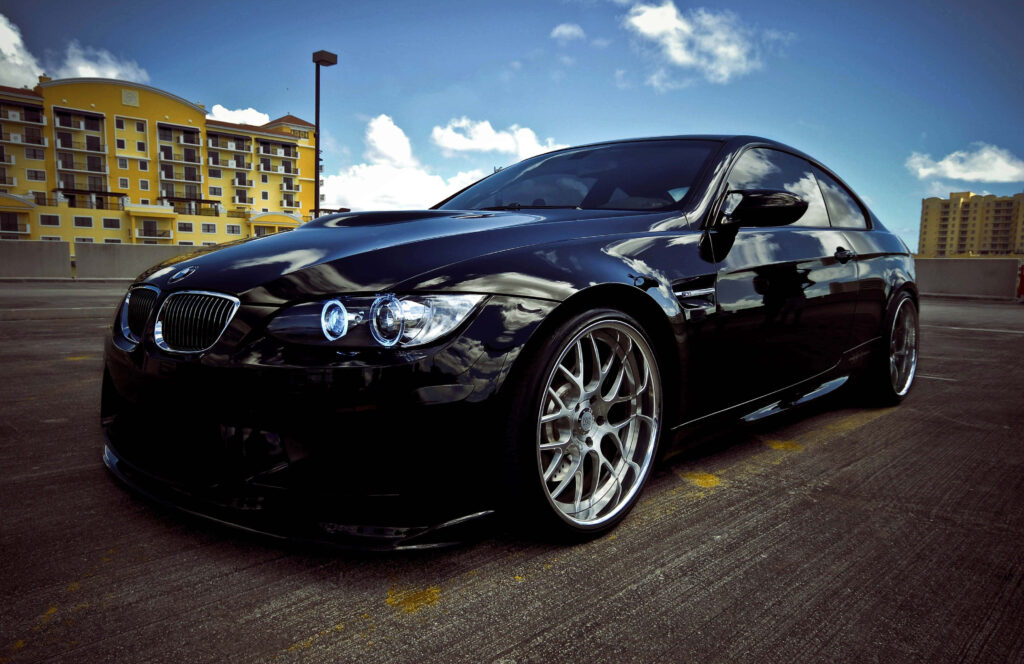 BMW M3 with glossy black paint and aggressive styling parked on urban rooftop under bright sky Wallpaper