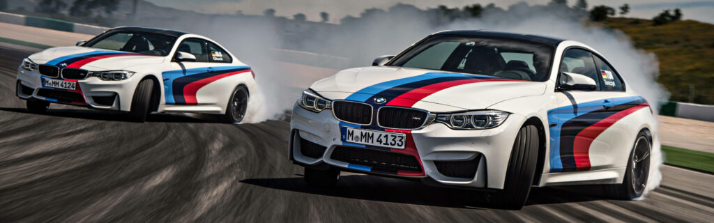 Two BMW M4 Drift Cars slide with tire smoke on race track capturing high-speed adrenaline action Wallpaper