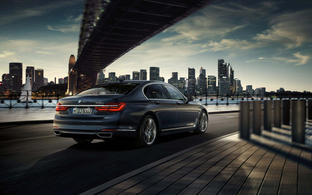 Sleek BMW driving riverside road city skyline impressive bridge urban luxury wallpaper background