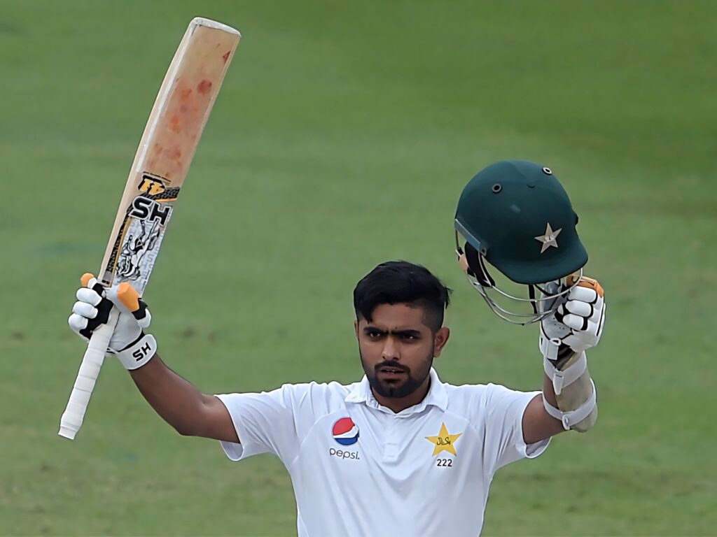 Babar Azam celebrates on cricket field wearing Pakistan Test uniform raising bat and helmet Wallpaper