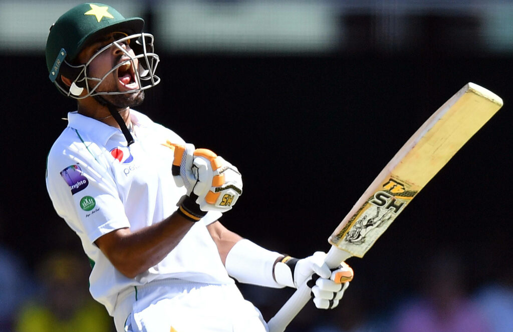 Babar Azam celebrating passionately in white cricket uniform on field background wallpaper