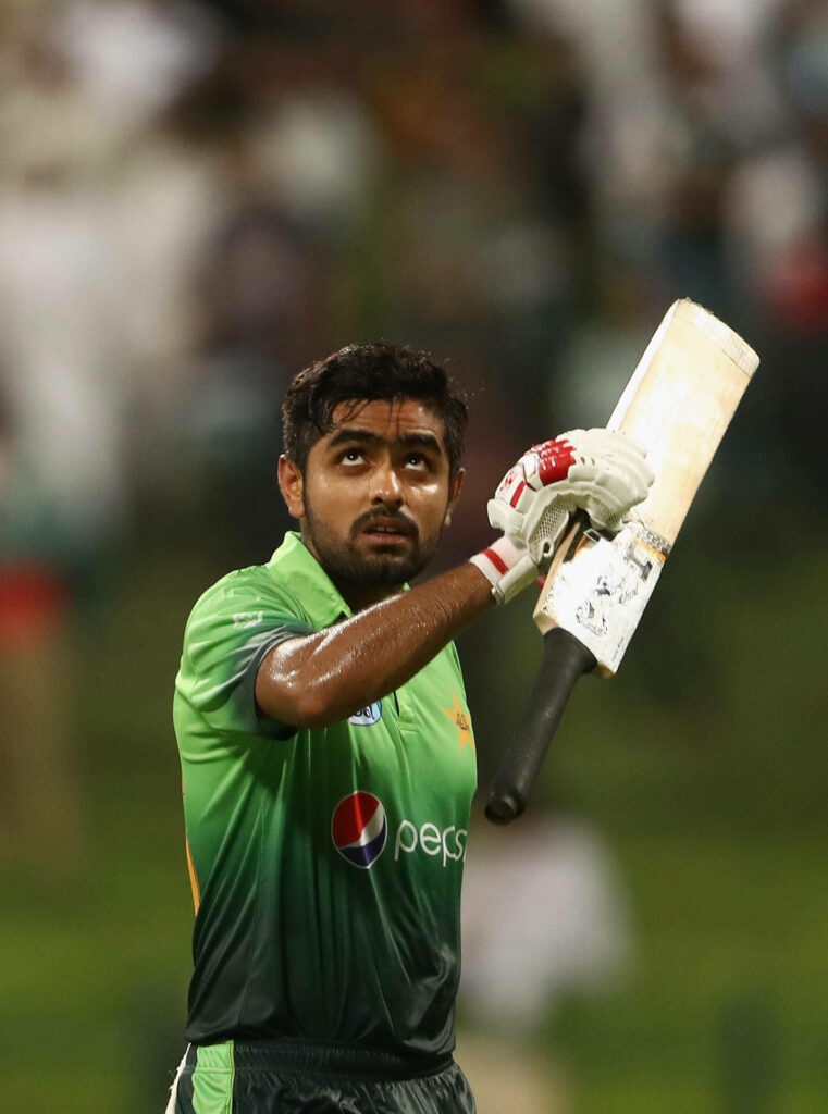 Babar Azam celebrates with raised cricket bat wearing Pakistan jersey on cricket field wallpaper background