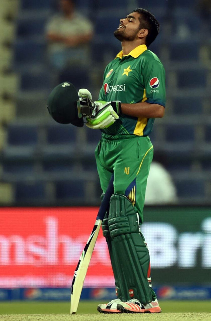 Babar Azam in green Pakistan cricket uniform holding bat and helmet with determined look Wallpaper