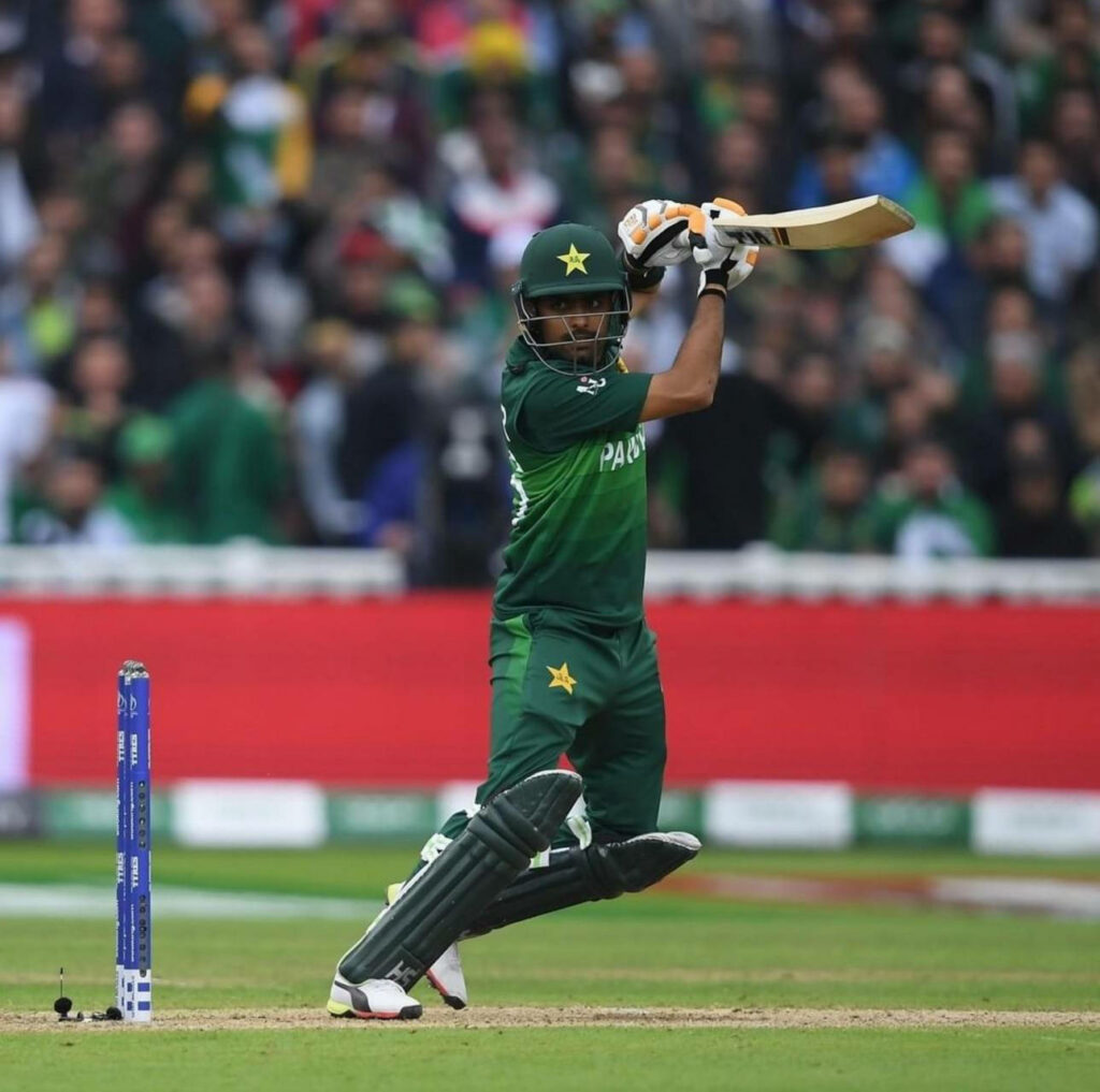 Babar Azam hitting a powerful cricket shot for Pakistan with focused crowd in stadium background Wallpaper