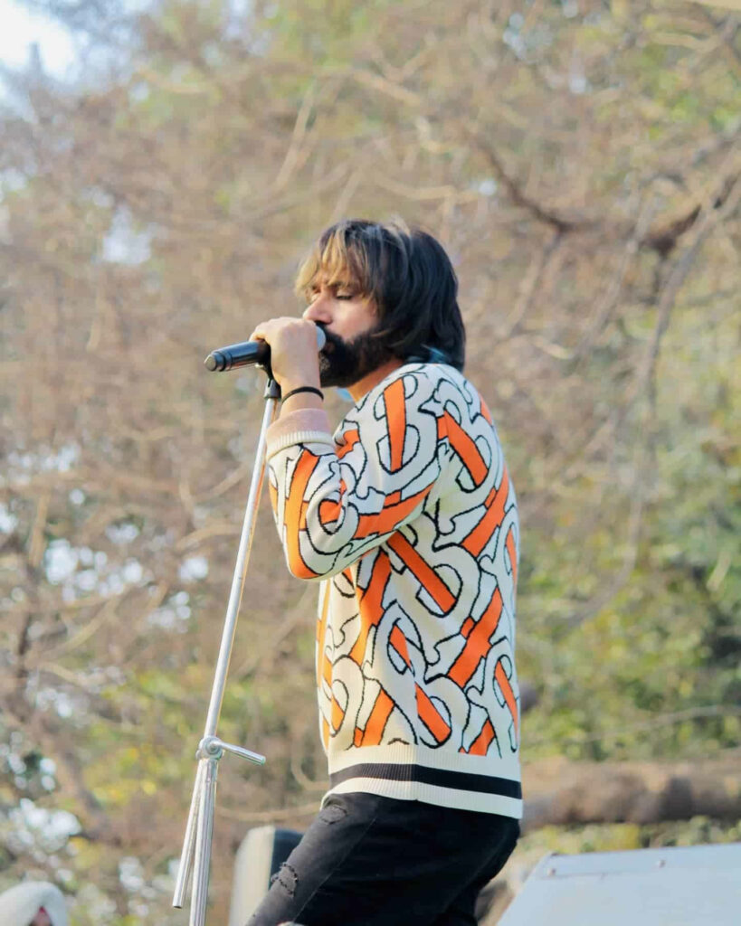 Babbu Maan singing passionately onstage with microphone and vibrant tree background wallpaper