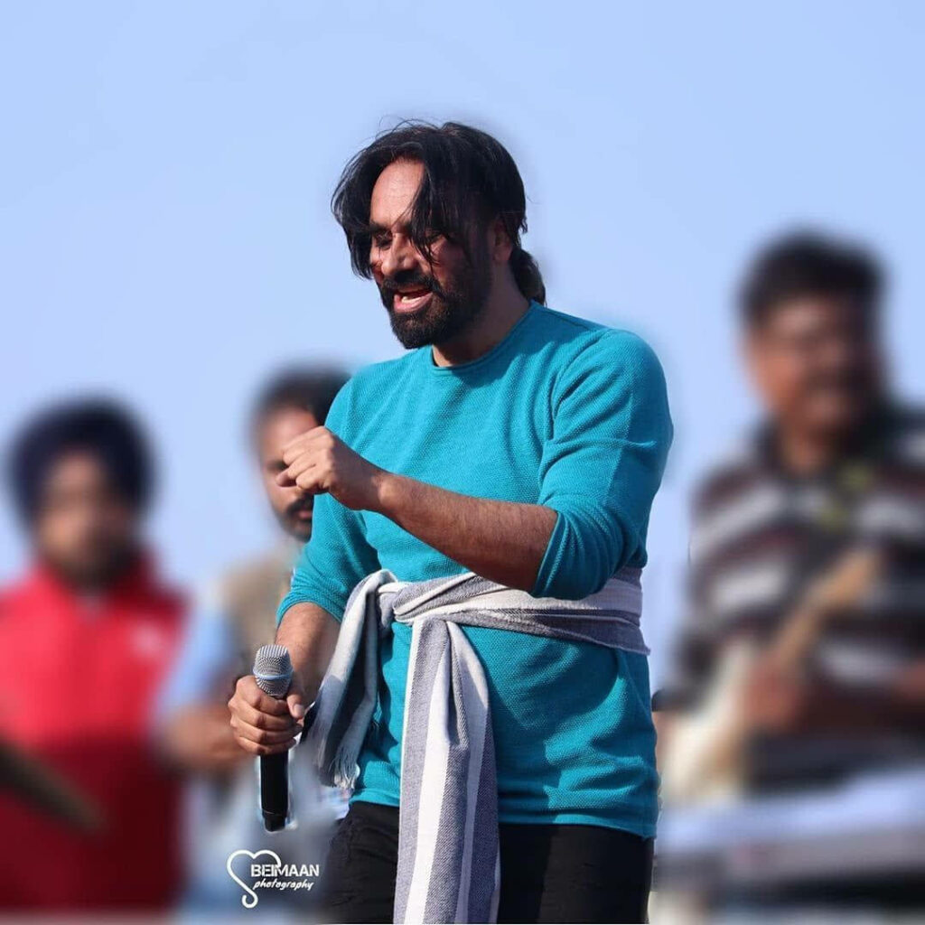 Babbu Maan performing live on stage in blue sweater with microphone and cheering audience Wallpaper