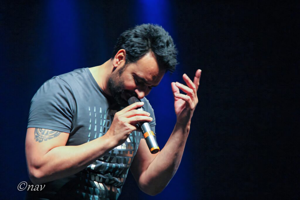 Babbu Maan performing live on stage with energetic passion and vibrant wallpaper background