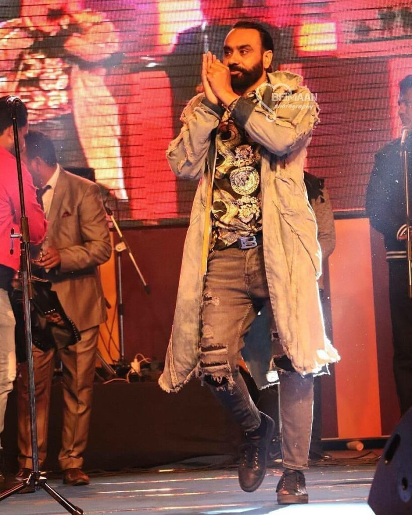 Babbu Maan performing live wearing long denim jacket ripped jeans vibrant stage lights concert Wallpaper