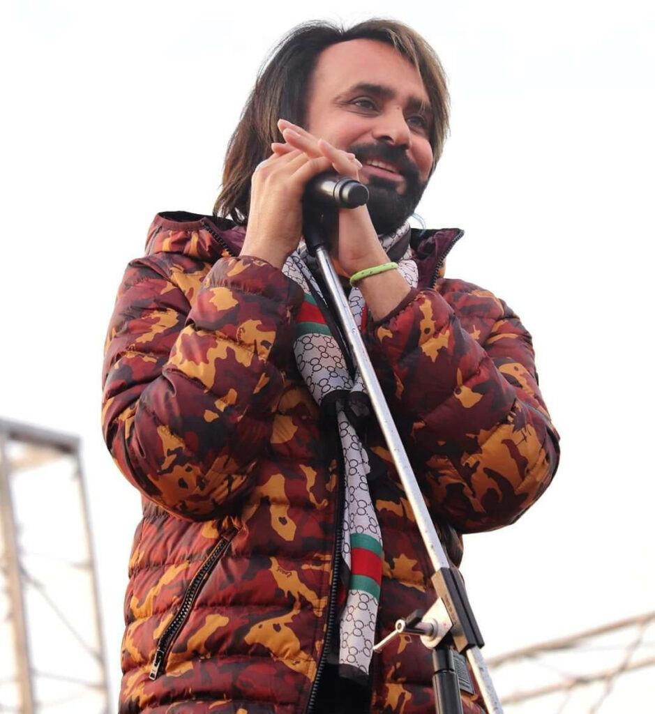 Babbu Maan performing live in stylish red puffy jacket on stage wallpaper background