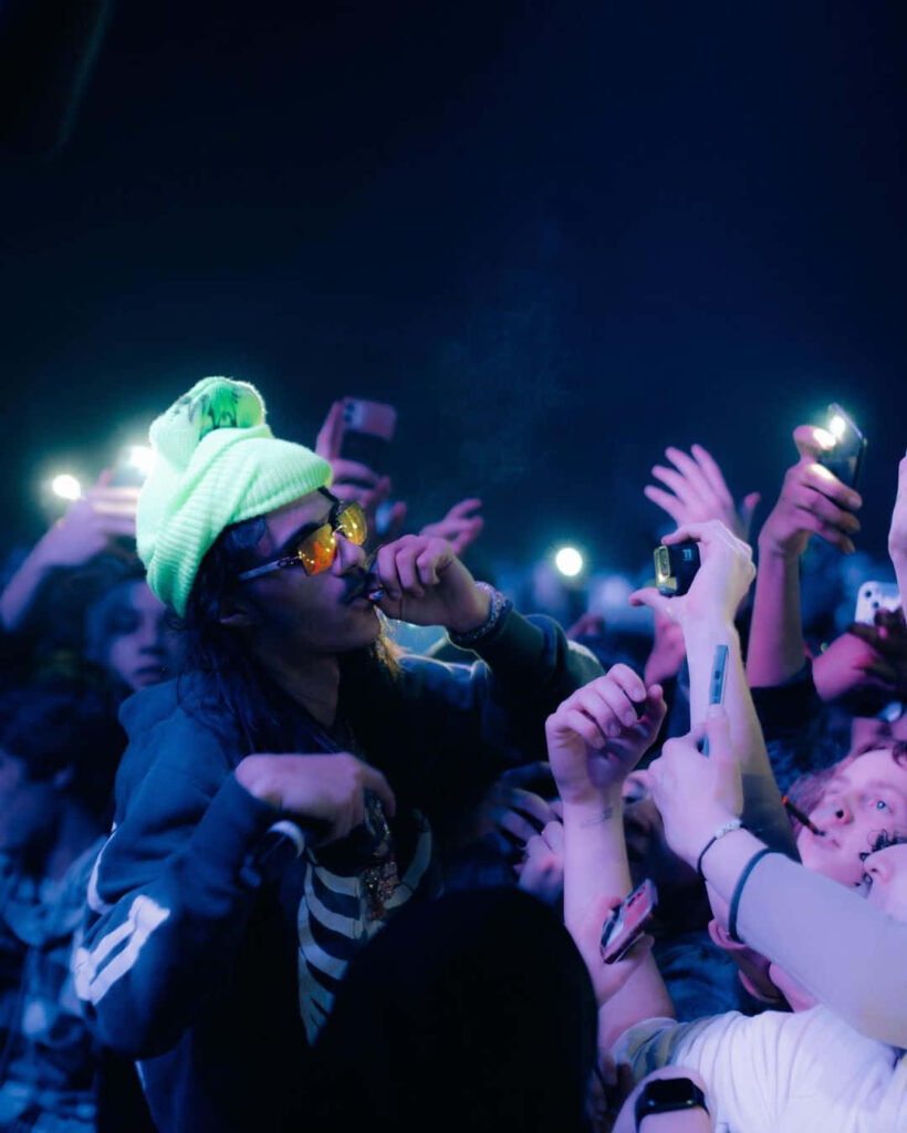 BabyTron raps on stage with glowing phone lights and excited fans reaching out in a vibrant crowd Wallpaper