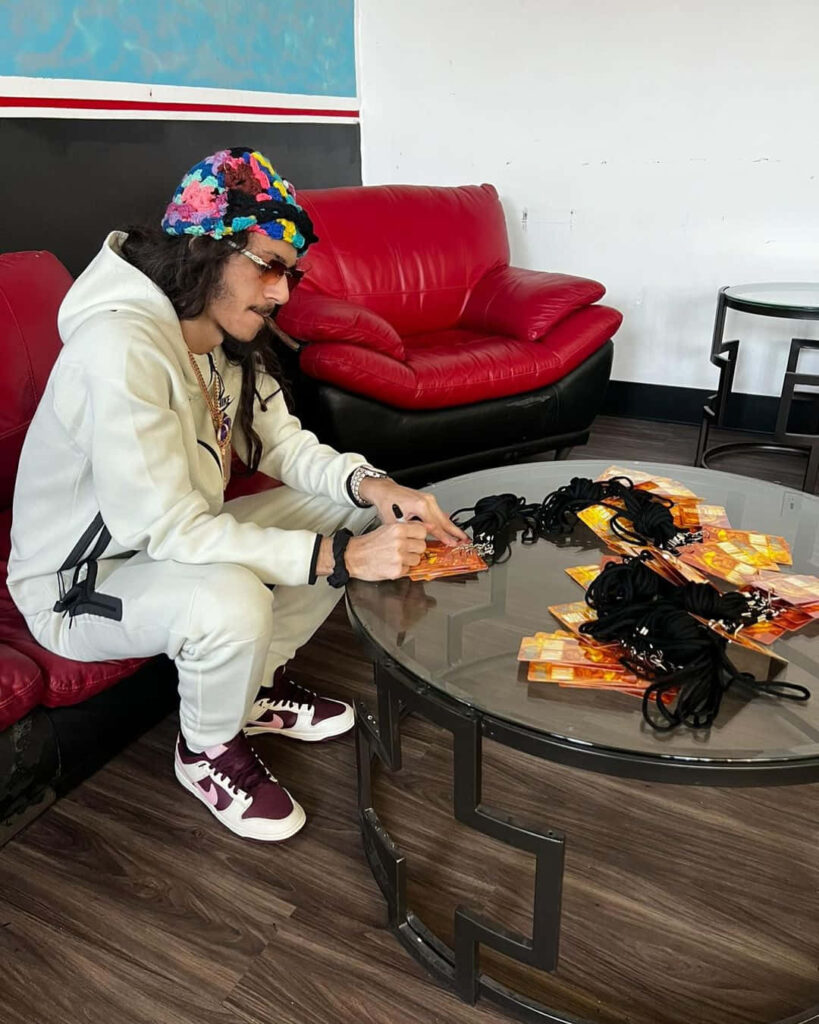BabyTron American rapper signing merchandise on glass table wearing white tracksuit colorful hat Wallpaper