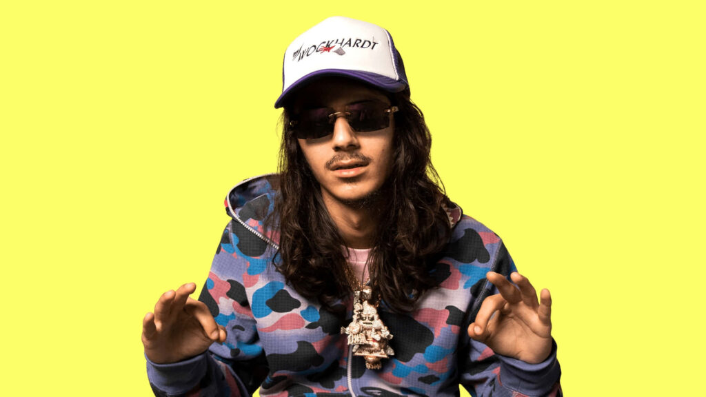 BabyTron American rapper in colorful camo hoodie sunglasses necklace and Tr0yward hat on yellow background Wallpaper