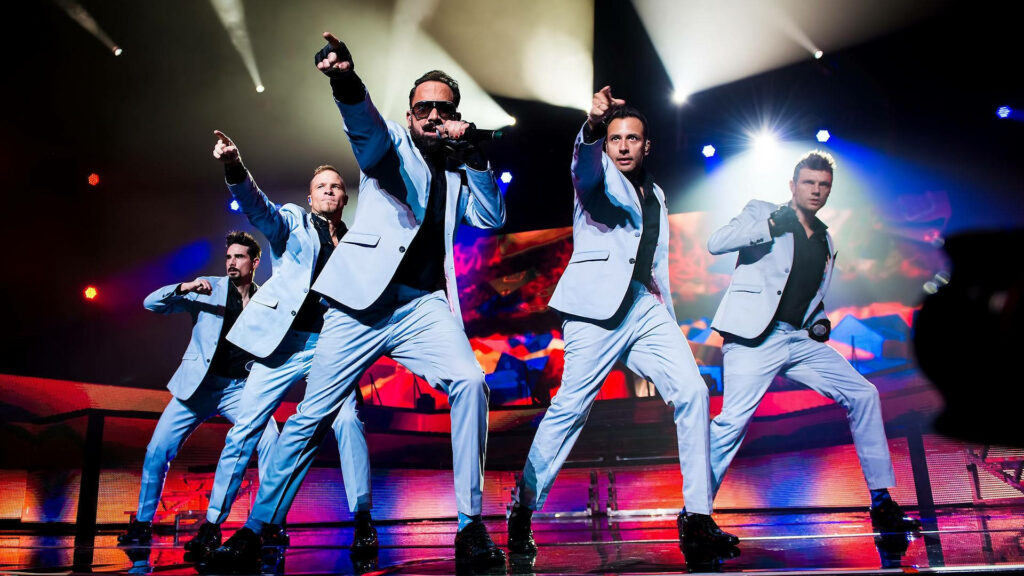 Backstreet Boys performing live on stage in matching blue suits with vibrant concert lights Wallpaper