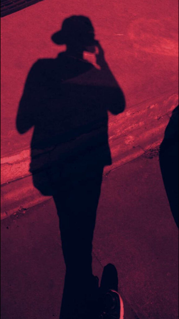 Backlit Coolness: A Stylish Shadow of a Boy with a Backward Hat against a Fiery Red Backdrop Wallpaper