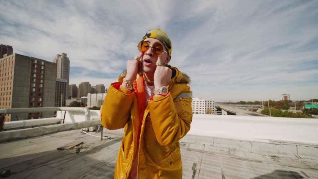 Bad Bunny on rooftop in vibrant orange outfit with jacket and accessories showcasing bold style Wallpaper