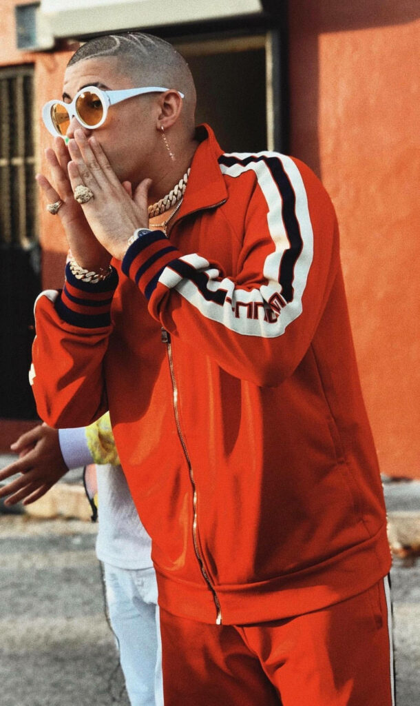 Bad Bunny surprised in red striped tracksuit sunglasses jewelry dynamic Puerto Rican rapper style Wallpaper
