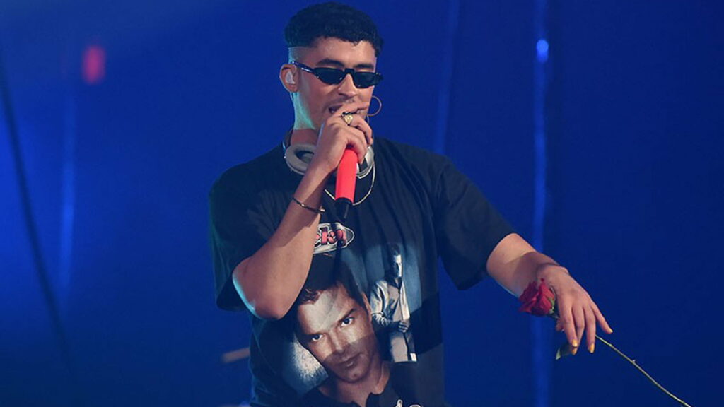 Melodic Maestro: Bad Bunny Dons Elegant Attire, Unleashing Powerful Vocals against a Serene Blue Backdrop Wallpaper