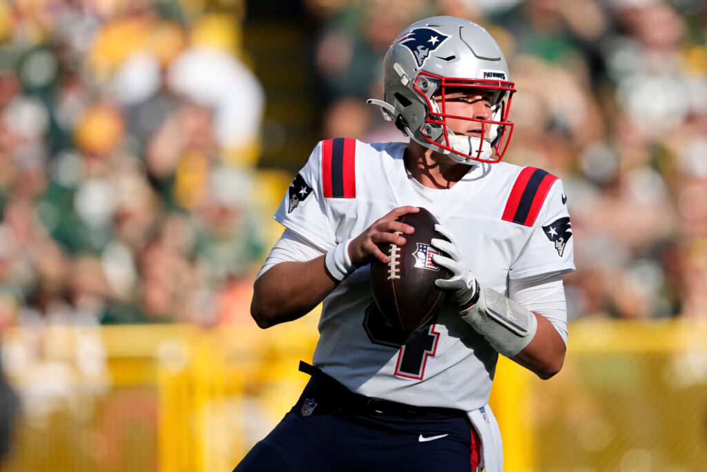 Bailey Zappe in New England Patriots uniform focused preparing to throw a pass during game Wallpaper