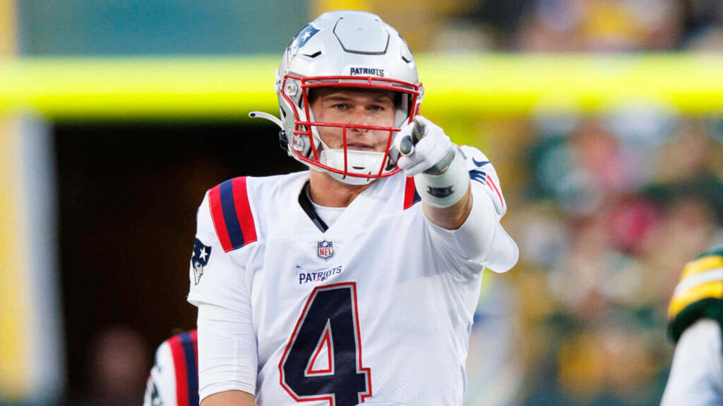 Bailey Zappe in New England Patriots uniform pointing confidently on football field wallpaper background