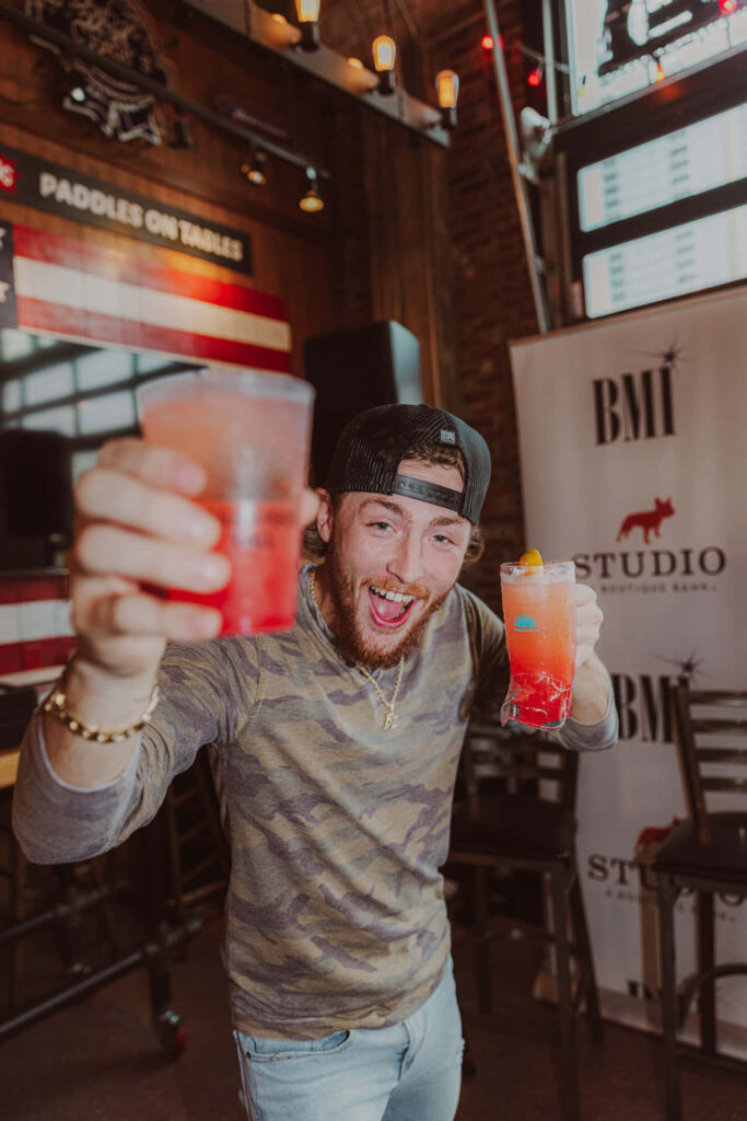 Bailey Zimmerman cheers with raised drink at lively event creating fun celebratory atmosphere wallpaper