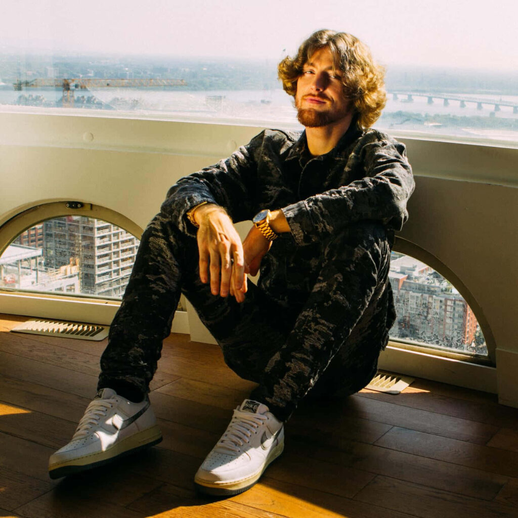 Bailey Zimmerman by city window in patterned outfit and white sneakers with sunlight glow wallpaper