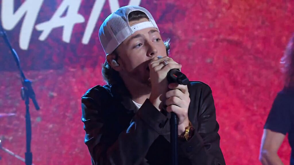 Bailey Zimmerman performing passionately on stage with vibrant red background country style wallpaper