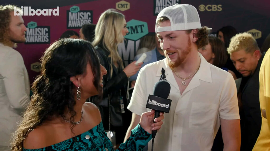 Bailey Zimmerman interviewed on red carpet at awards event with lively crowd and branding backdrop Wallpaper