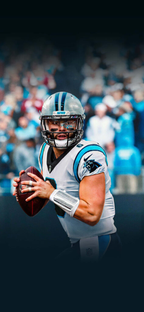Baker Mayfield in Carolina Panthers uniform preparing to throw football with cheering crowd background Wallpaper