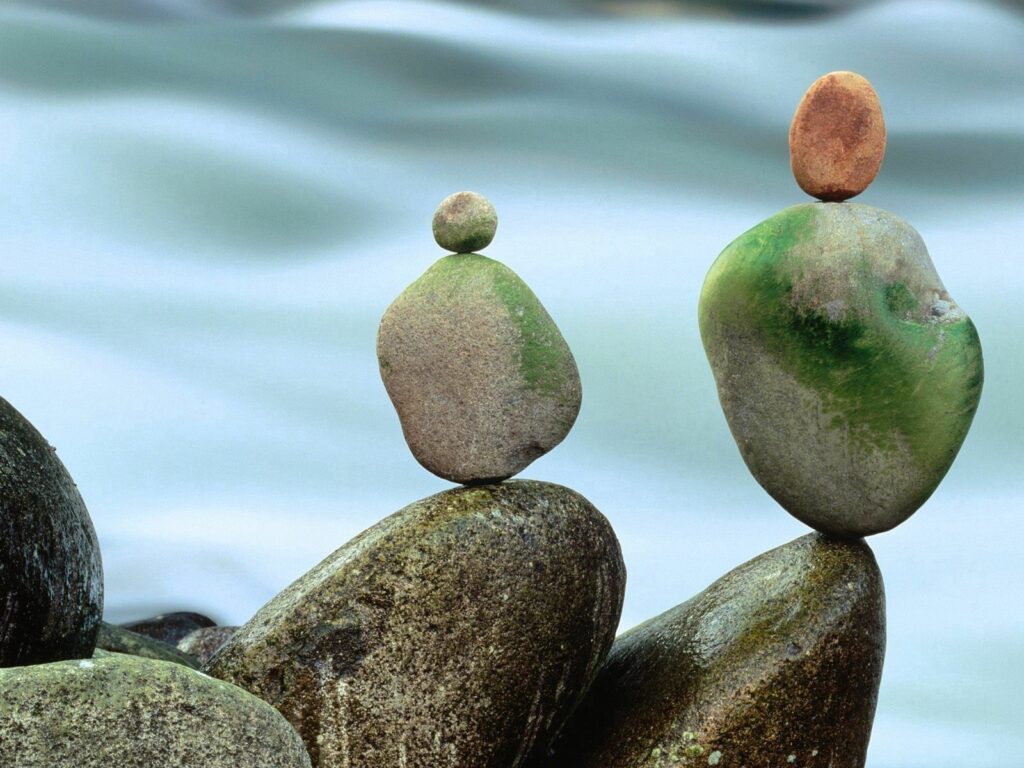 Stacked smooth gray and green stones balanced by calm water for serene tranquil wallpaper background