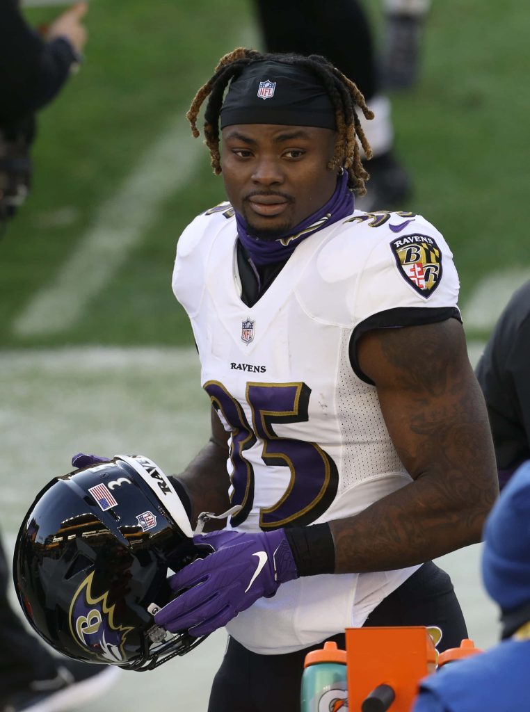 Baltimore Ravens Gus Edwards in white jersey 35 holding helmet on field NFL football wallpaper
