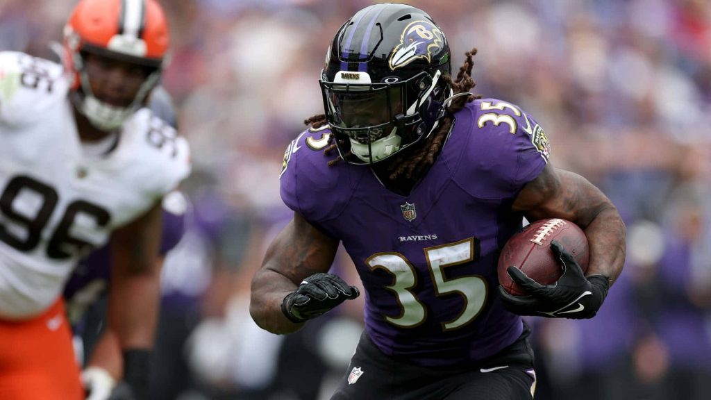 Baltimore Ravens running back Gus Edwards in purple jersey powering forward on NFL game field Wallpaper
