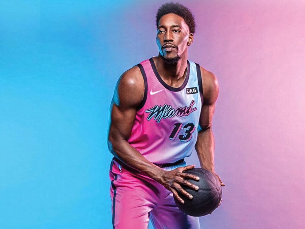 Bam Adebayo in Miami Heat jersey holding basketball with blue and pink gradient background Wallpaper