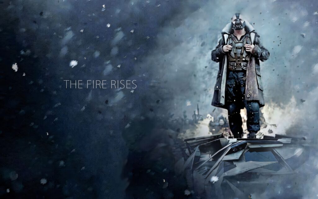 Bane stands amid falling ash with The Fire Rises text in dramatic DC Comics cinematic wallpaper background
