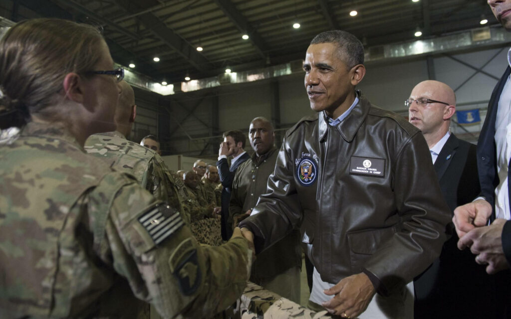 Barack Obama in commander in chief jacket shaking hands with military personnel in hangar Wallpaper