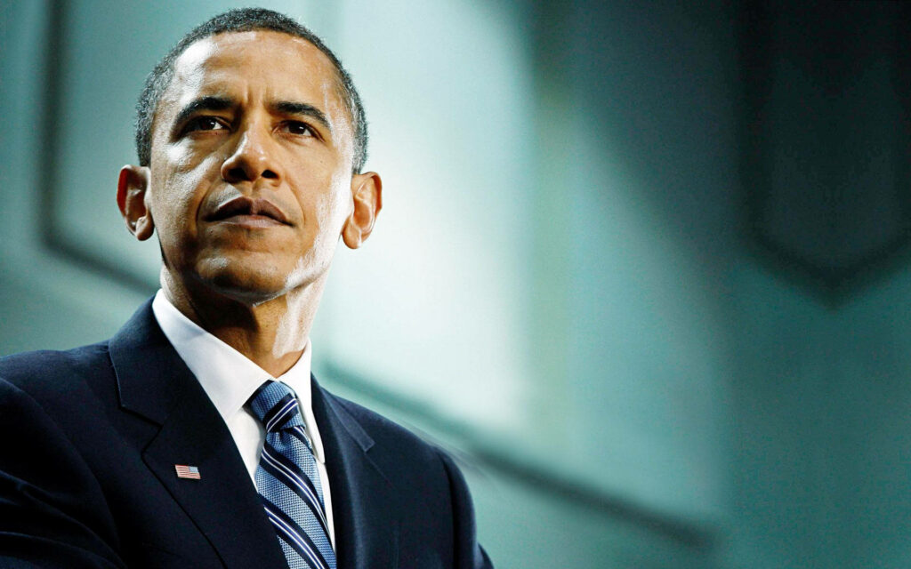 Barack Obama in formal suit with serious expression against softly lit wallpaper background