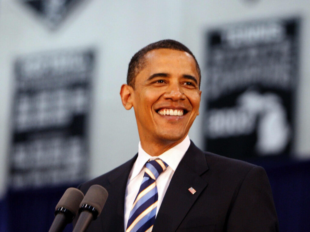 Barack Obama smiling warmly speaking at event wearing suit striped tie with banner backdrop wallpaper