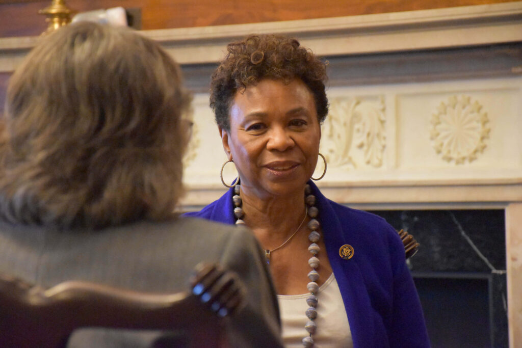 Barbara Lee in thoughtful conversation with a woman in formal setting with wallpaper background