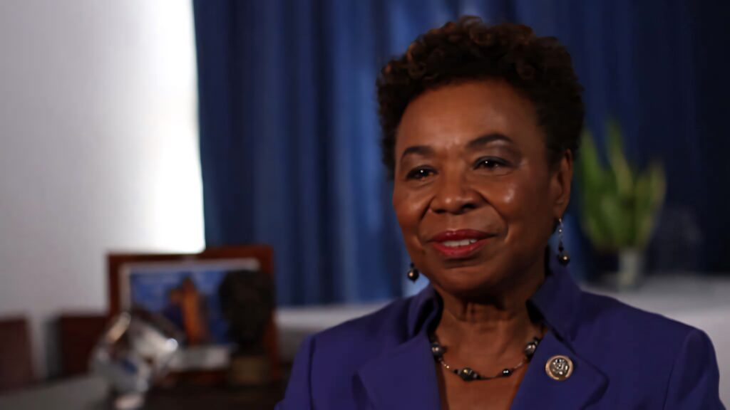 Barbara Lee smiling in professional interview wearing blue blazer with blue curtain office background Wallpaper