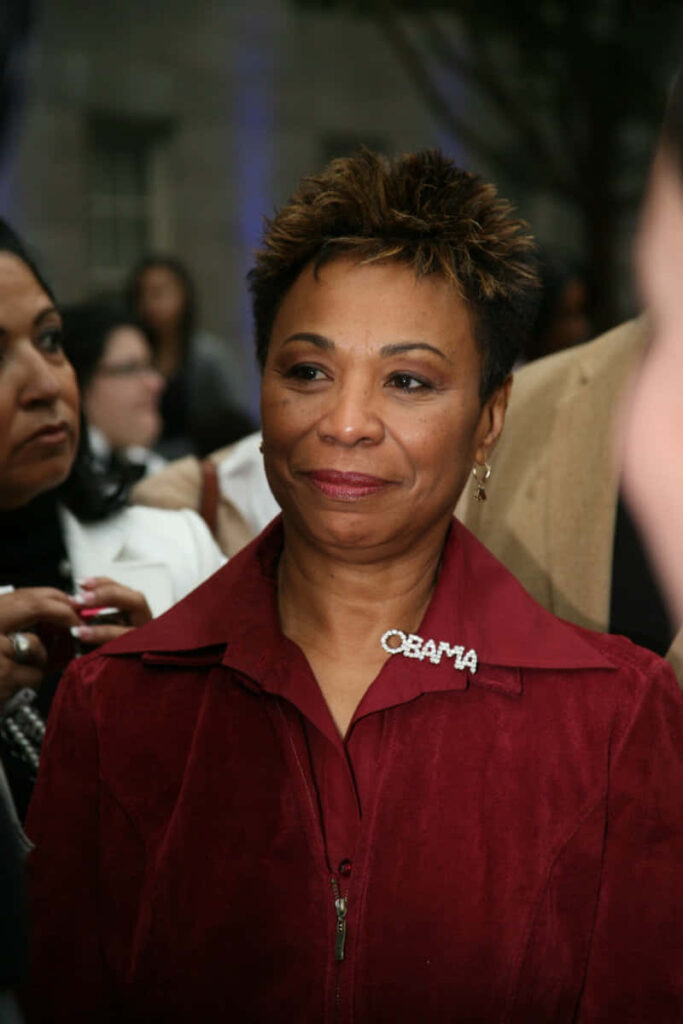Barbara Lee in red jacket with Obama pin at public event against wallpaper background